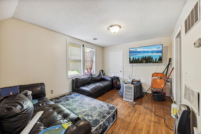 living room featuring a textured ceiling, hardwood / wood-style flooring, heating unit, and lofted ceiling