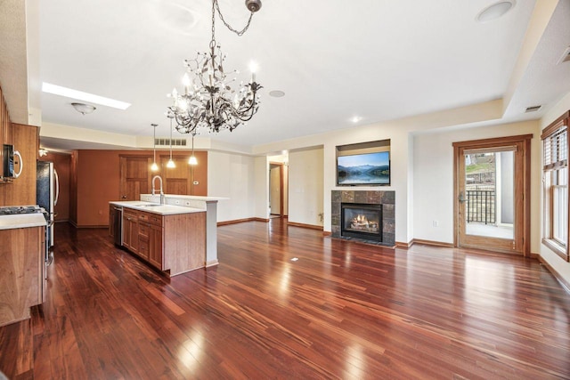 kitchen featuring a kitchen island with sink, sink, dark hardwood / wood-style floors, hanging light fixtures, and a tiled fireplace