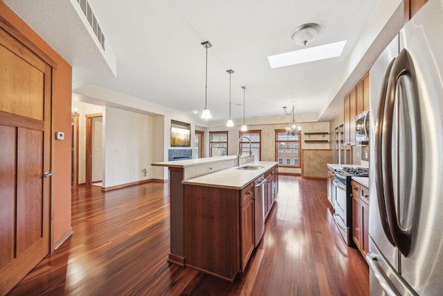 kitchen with appliances with stainless steel finishes, a skylight, a kitchen island with sink, sink, and decorative light fixtures