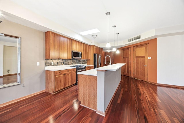 kitchen featuring backsplash, a skylight, an island with sink, appliances with stainless steel finishes, and decorative light fixtures