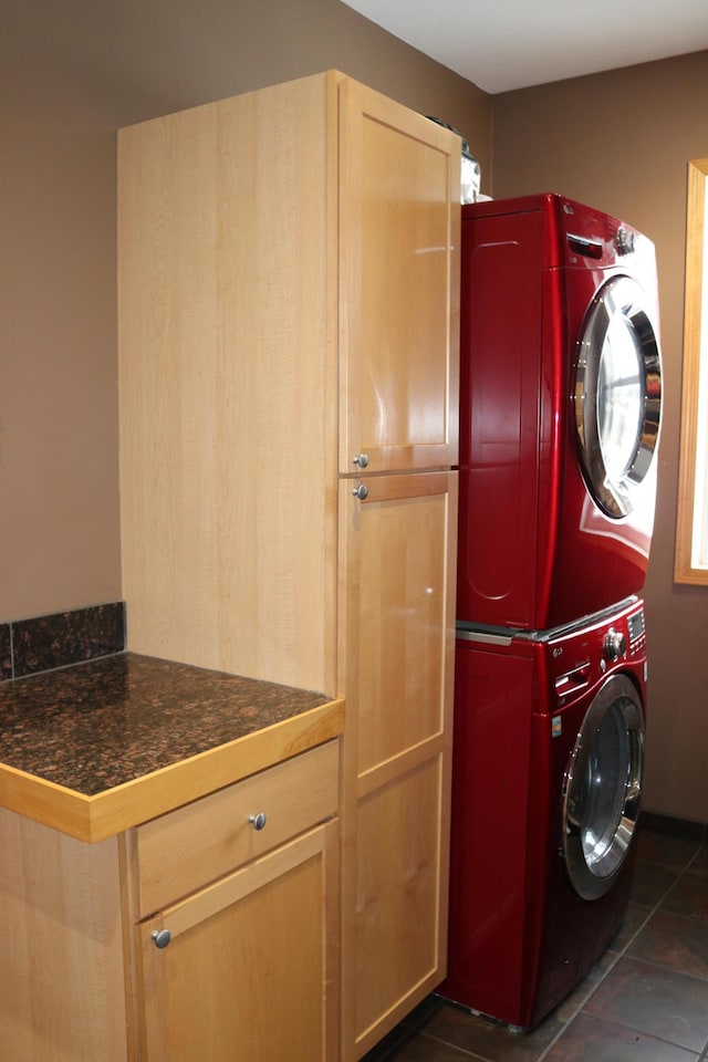 washroom featuring cabinets, dark tile patterned floors, and stacked washer and dryer