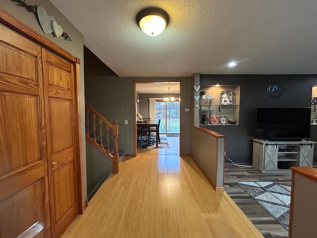 hallway with light wood-type flooring, a textured ceiling, and an inviting chandelier