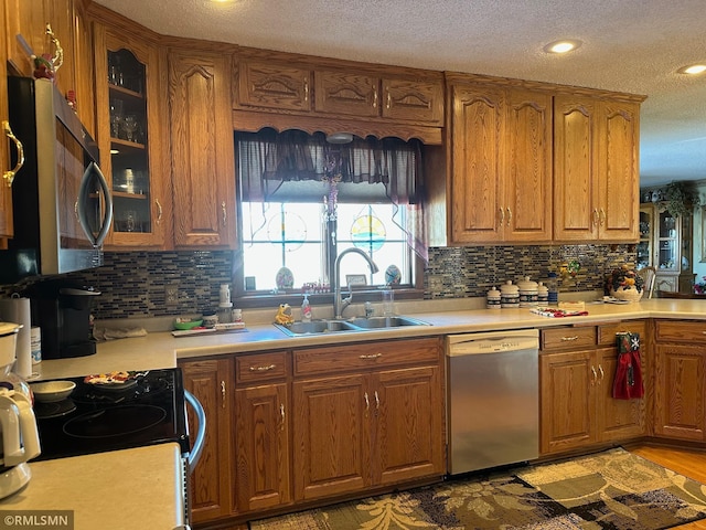 kitchen featuring a sink, glass insert cabinets, brown cabinetry, a textured ceiling, and appliances with stainless steel finishes