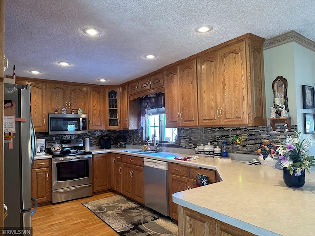 kitchen with stainless steel appliances, a sink, a textured ceiling, tasteful backsplash, and brown cabinets