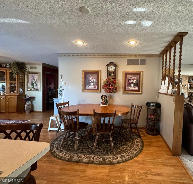 dining space with wood finished floors, a textured ceiling, and visible vents