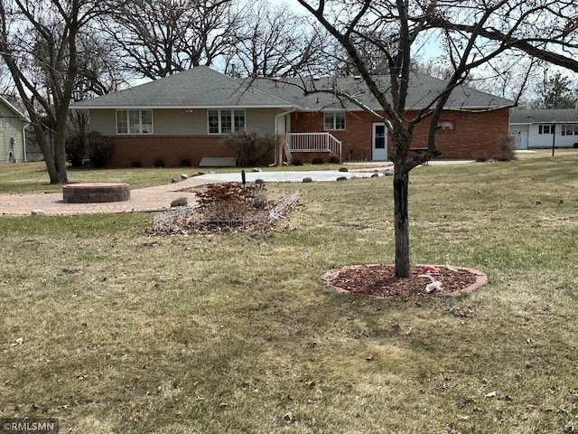 ranch-style home featuring brick siding, a front yard, and an outdoor fire pit