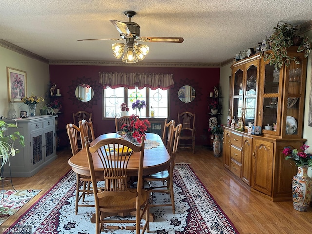 dining area featuring light wood-style flooring, a textured ceiling, crown molding, and ceiling fan