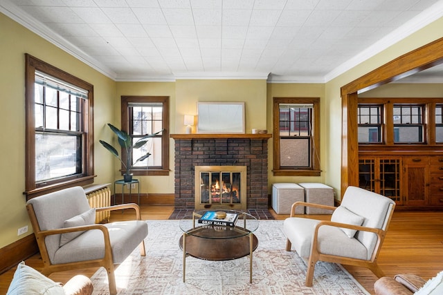 living area with light wood-type flooring, a brick fireplace, and crown molding