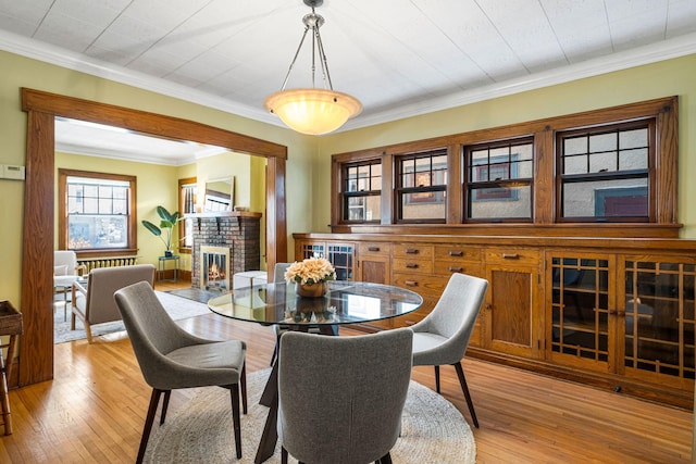 dining room featuring ornamental molding, a fireplace, and light hardwood / wood-style flooring