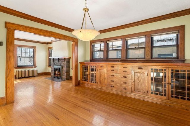 unfurnished living room featuring a fireplace, radiator heating unit, ornamental molding, and wood-type flooring