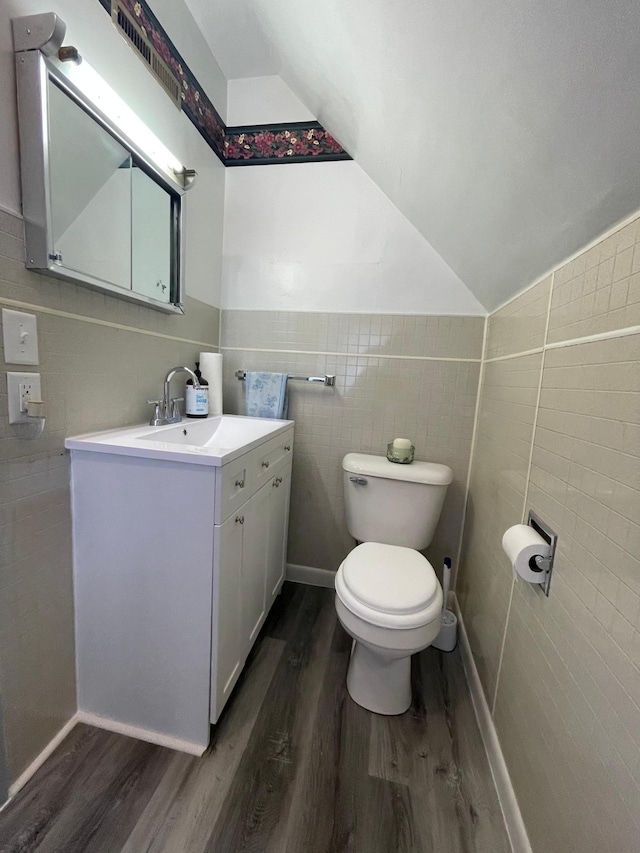 bathroom with vanity, vaulted ceiling, wood-type flooring, tile walls, and toilet