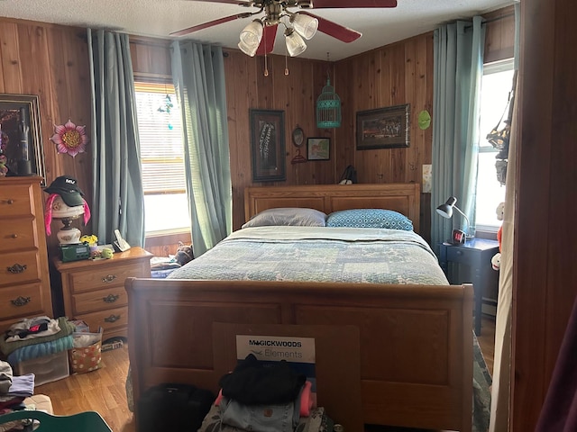 bedroom featuring a textured ceiling, hardwood / wood-style flooring, ceiling fan, and wood walls