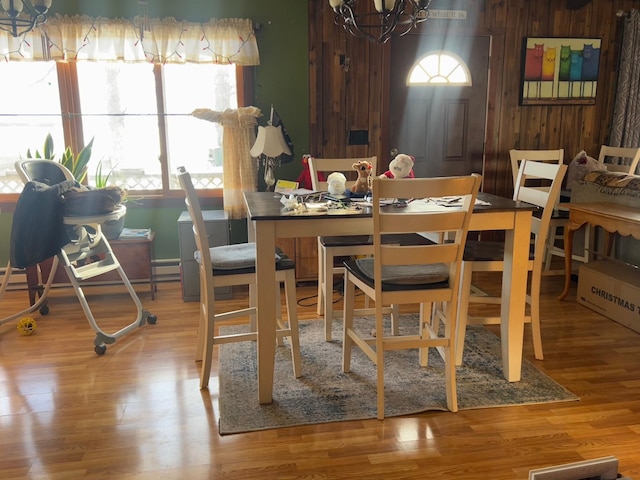 dining room with light wood-type flooring, a notable chandelier, and wood walls