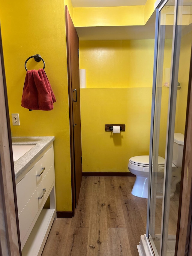 bathroom featuring hardwood / wood-style floors, vanity, a shower with door, and toilet