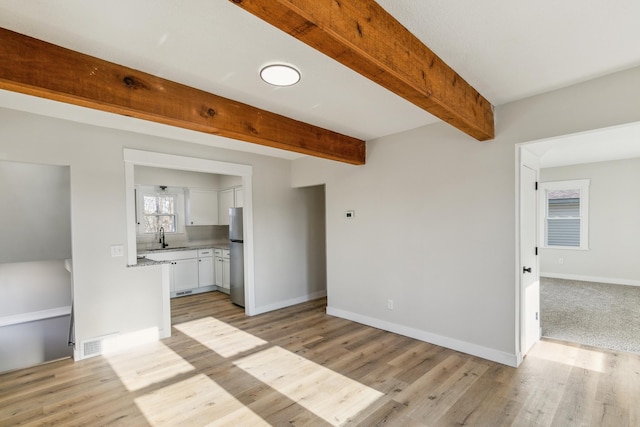 unfurnished living room featuring beamed ceiling, light hardwood / wood-style floors, and sink