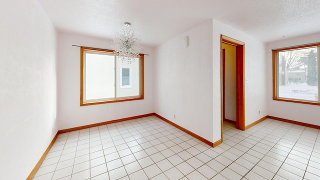 tiled empty room featuring a textured ceiling and an inviting chandelier