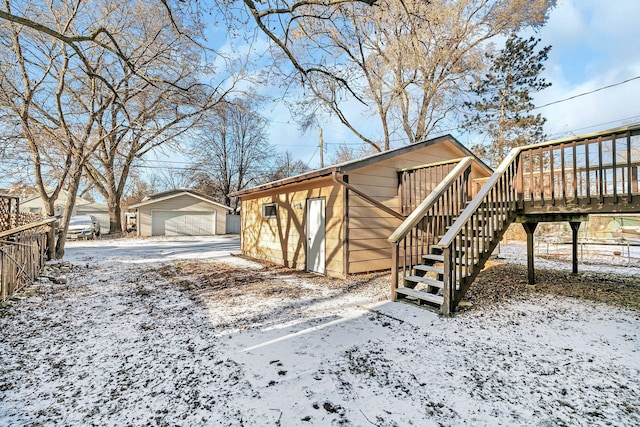 yard covered in snow featuring a deck, a garage, and an outbuilding