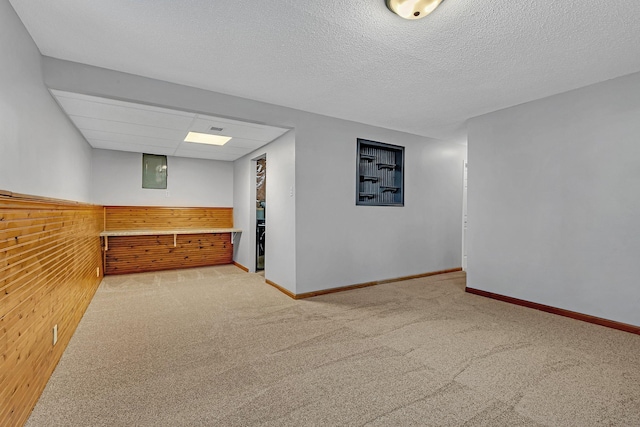 spare room with light colored carpet, wood walls, a textured ceiling, and electric panel