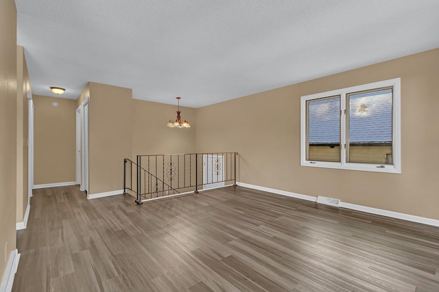 spare room with baseboards, a chandelier, wood finished floors, and visible vents
