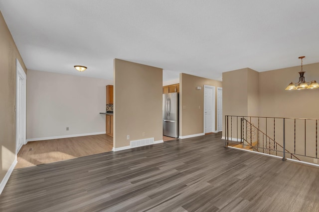 unfurnished room with baseboards, visible vents, dark wood finished floors, and a notable chandelier