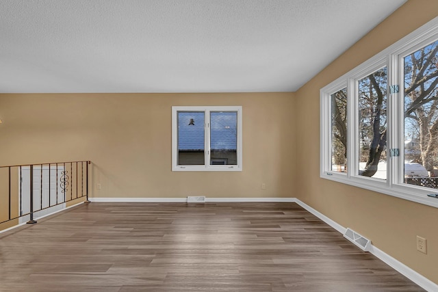 empty room with a textured ceiling, baseboards, visible vents, and wood finished floors