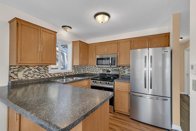 kitchen with dark countertops, a sink, stainless steel appliances, a peninsula, and wood finished floors