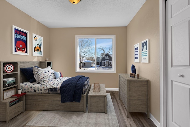 bedroom with a textured ceiling, baseboards, and wood finished floors