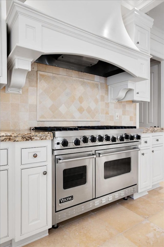 kitchen with premium range hood, white cabinetry, decorative backsplash, range with two ovens, and light stone counters