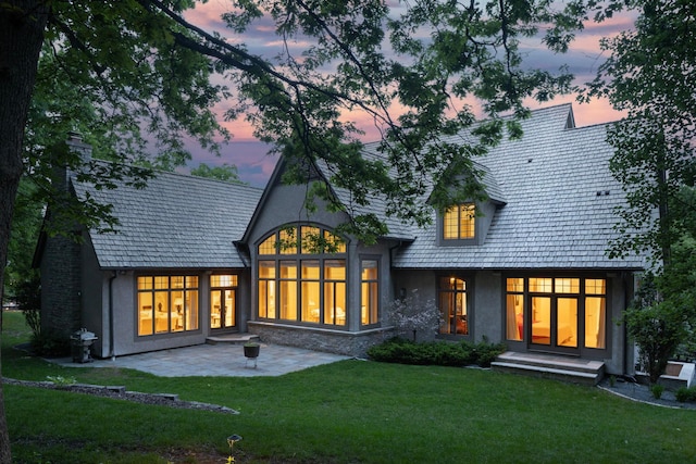 back house at dusk with a patio area and a lawn