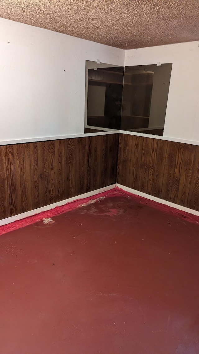 empty room featuring concrete flooring, a textured ceiling, and wooden walls