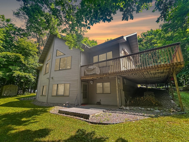 back house at dusk with a patio, a wooden deck, and a lawn