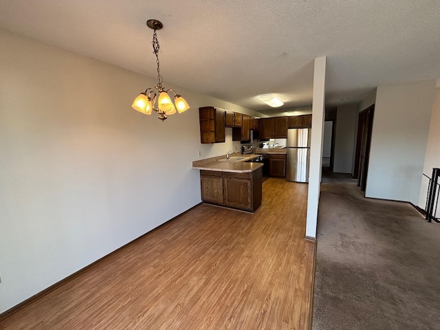 kitchen featuring decorative light fixtures, sink, stainless steel fridge, dark brown cabinets, and light wood-type flooring