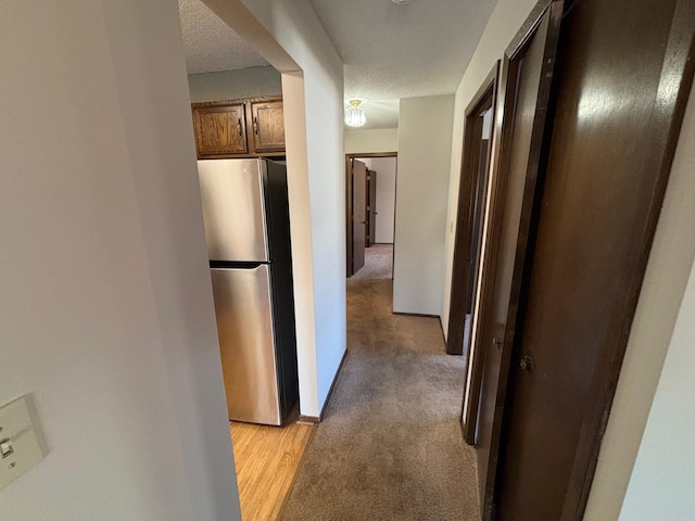 hallway with light colored carpet and a textured ceiling