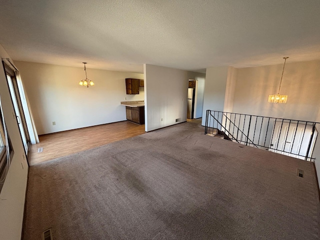 unfurnished living room with a textured ceiling, carpet floors, and a chandelier