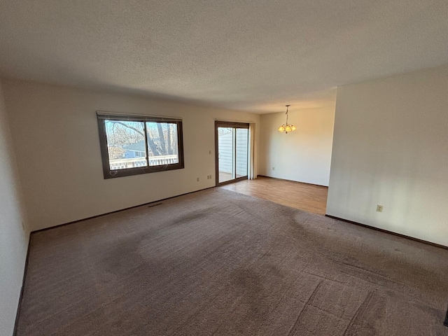 empty room with a notable chandelier, carpet floors, and a textured ceiling