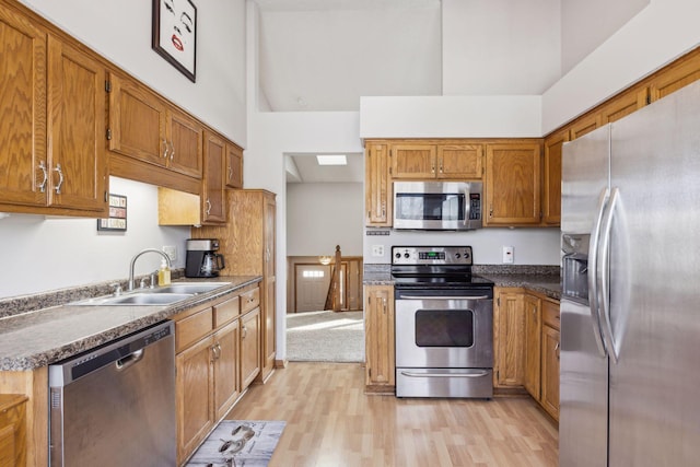 kitchen with light wood-type flooring, appliances with stainless steel finishes, sink, and a high ceiling