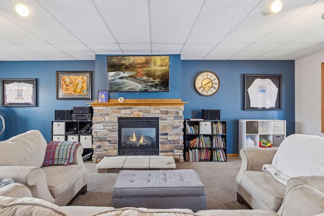 living room featuring carpet floors, a stone fireplace, and a drop ceiling