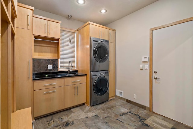 clothes washing area with cabinets, stacked washing maching and dryer, and sink