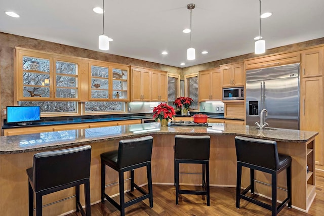 kitchen with sink, hanging light fixtures, built in appliances, a kitchen island with sink, and light wood-type flooring