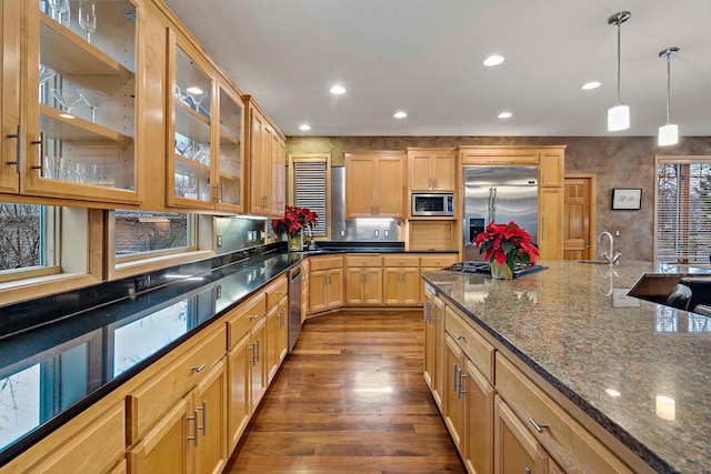 kitchen featuring dark wood-type flooring, sink, built in appliances, dark stone countertops, and hanging light fixtures