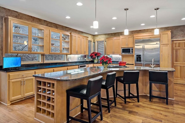 kitchen with light wood-type flooring, pendant lighting, built in appliances, and a center island with sink