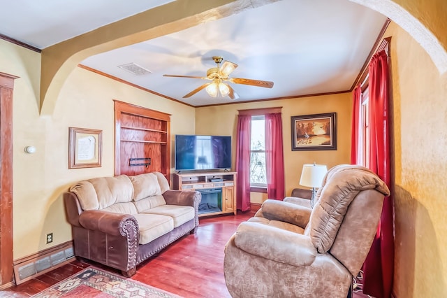 living room with hardwood / wood-style flooring, ceiling fan, ornamental molding, and a fireplace