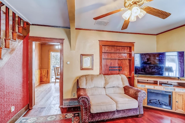 living room featuring beamed ceiling, light wood-type flooring, ceiling fan, and crown molding