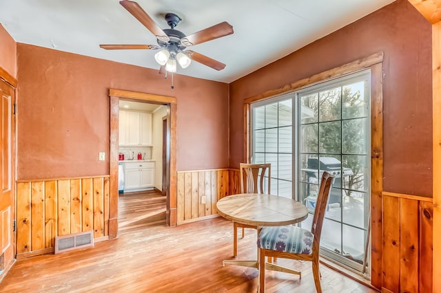 living area with ceiling fan, light hardwood / wood-style flooring, and wood walls