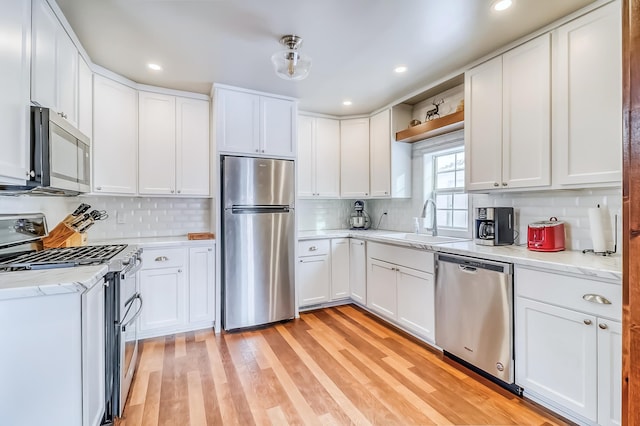 kitchen featuring backsplash, white cabinets, sink, light hardwood / wood-style floors, and stainless steel appliances