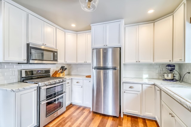 kitchen featuring decorative backsplash, light hardwood / wood-style floors, light stone counters, white cabinetry, and stainless steel appliances