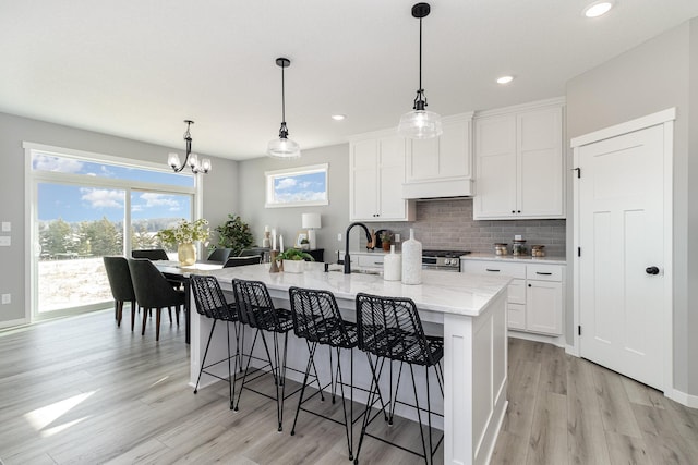 kitchen with white cabinetry, decorative light fixtures, an island with sink, and tasteful backsplash