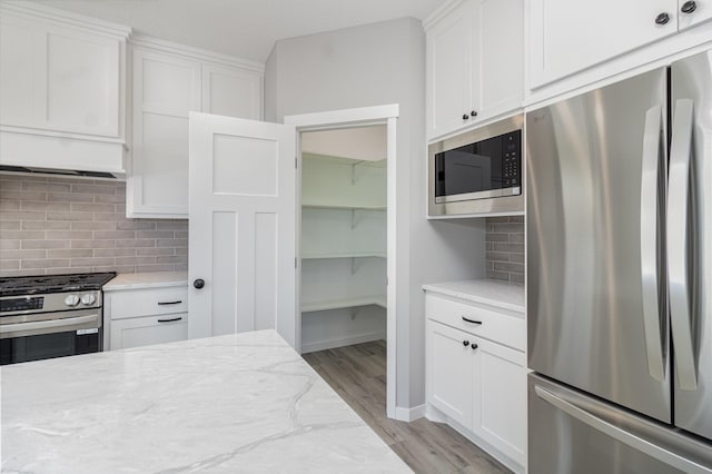 kitchen featuring light wood-type flooring, light stone countertops, white cabinets, and appliances with stainless steel finishes