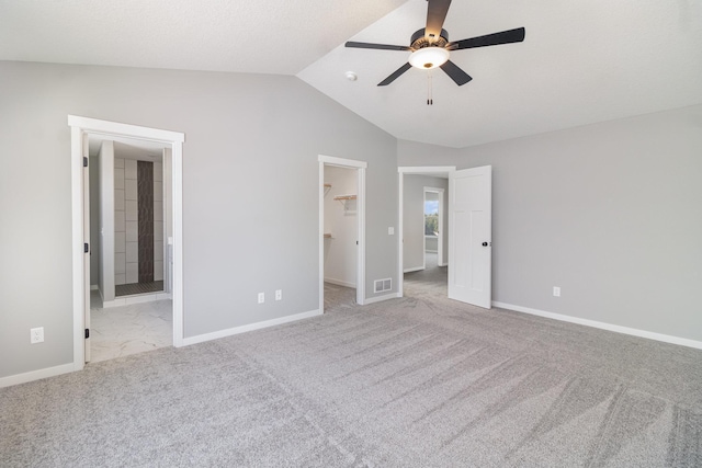 unfurnished bedroom featuring vaulted ceiling, ensuite bathroom, a walk in closet, light carpet, and a closet