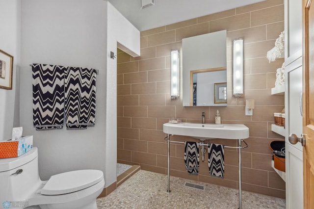 bathroom with sink, walk in shower, tile patterned flooring, toilet, and tile walls